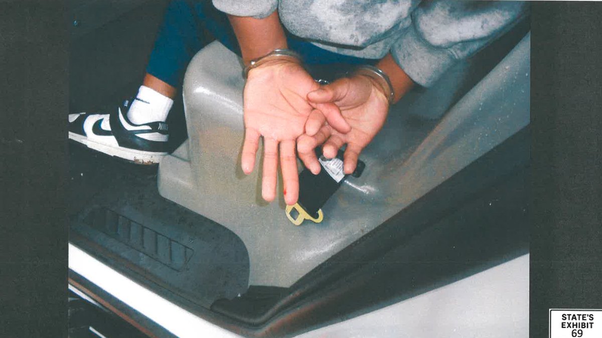 Karmelo Anthony is photographed handcuffed in a police vehicle with blood visible on his left-hand finger.