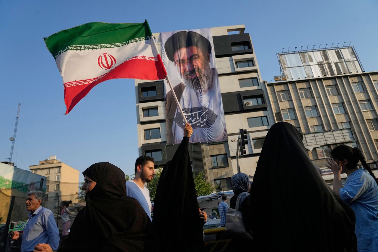 A woman holds up an Iranian flag in front of a banner showing the Supreme Leader Ayatollah Mojtaba Khamenei during a street festival celebrating Eid al-Ghadir, in Tehran, Iran, on Thursday, June 4.