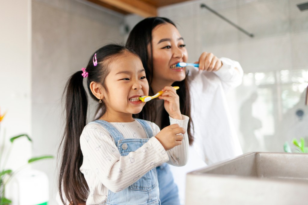 A Korean mother and daughter brushing their teeth in the bathroom together.