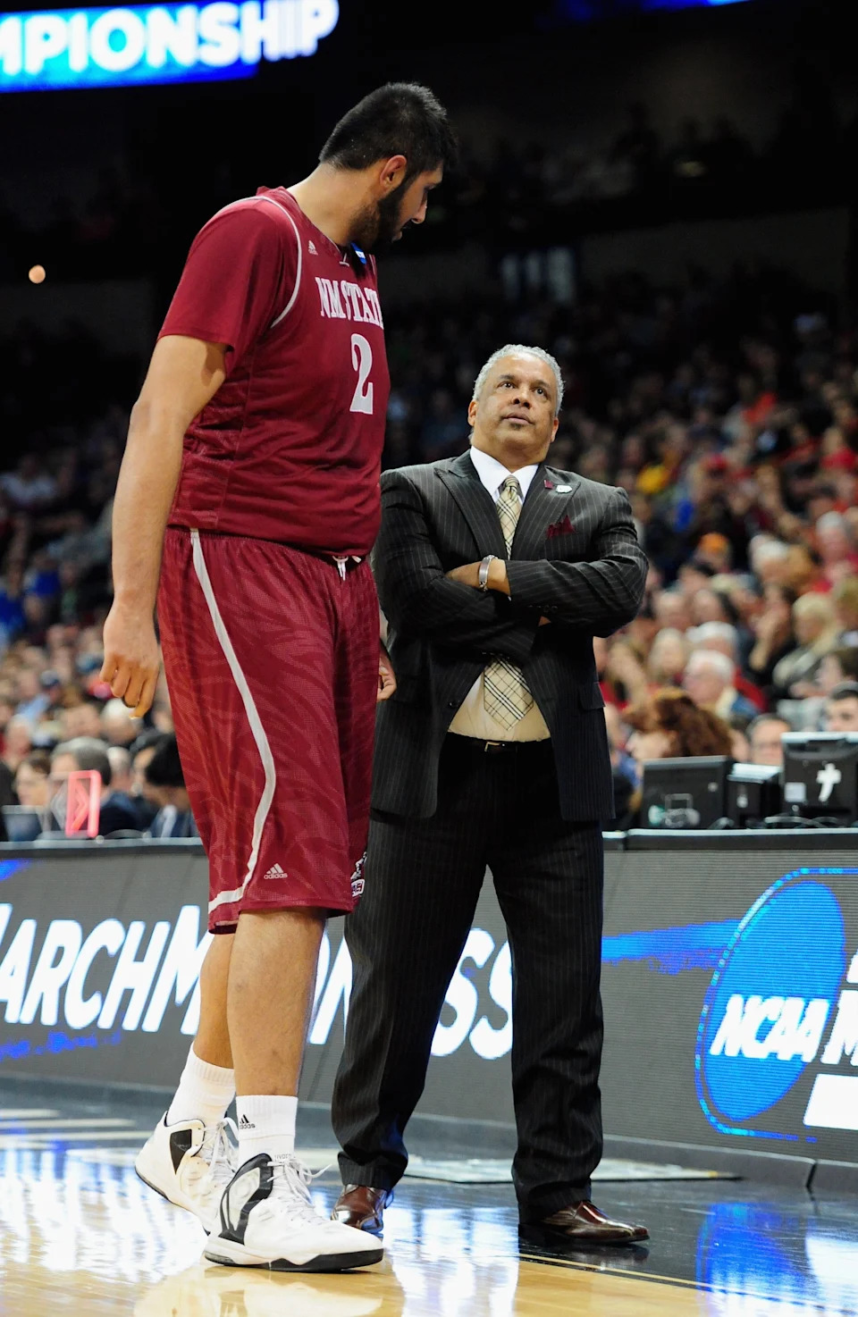 Basketball player in uniform chats with coach in a suit on court during a game
