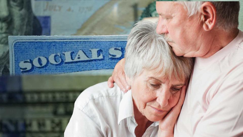 An older man, with a mustache and wearing a light-colored shirt, gently rests his forehead on the head of an older woman with short grey hair. His arm is around her shoulder in a comforting gesture. The woman looks down with a pensive expression, her hand touching her face. In the blurred background, a blue card with the word 'SOCIALS' partially visible and a hint of a dollar bill are seen, suggesting a connection to Social Security.