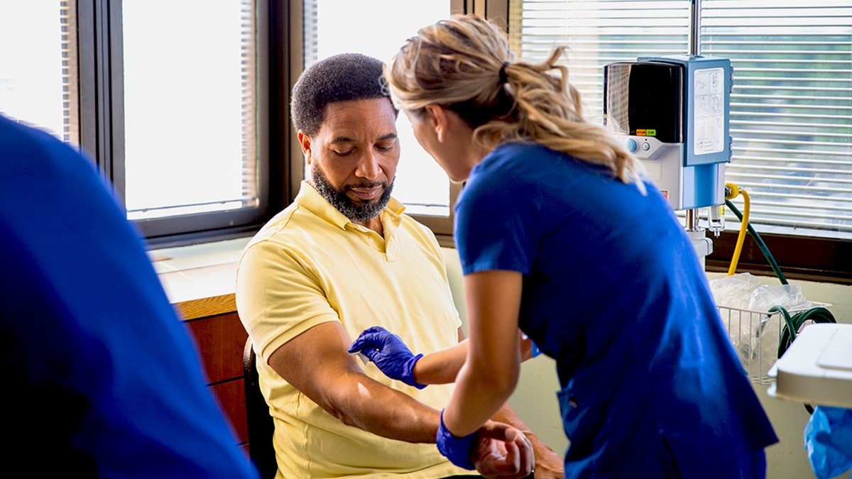 Man having blood drawn by a female nurse in a hospital setting