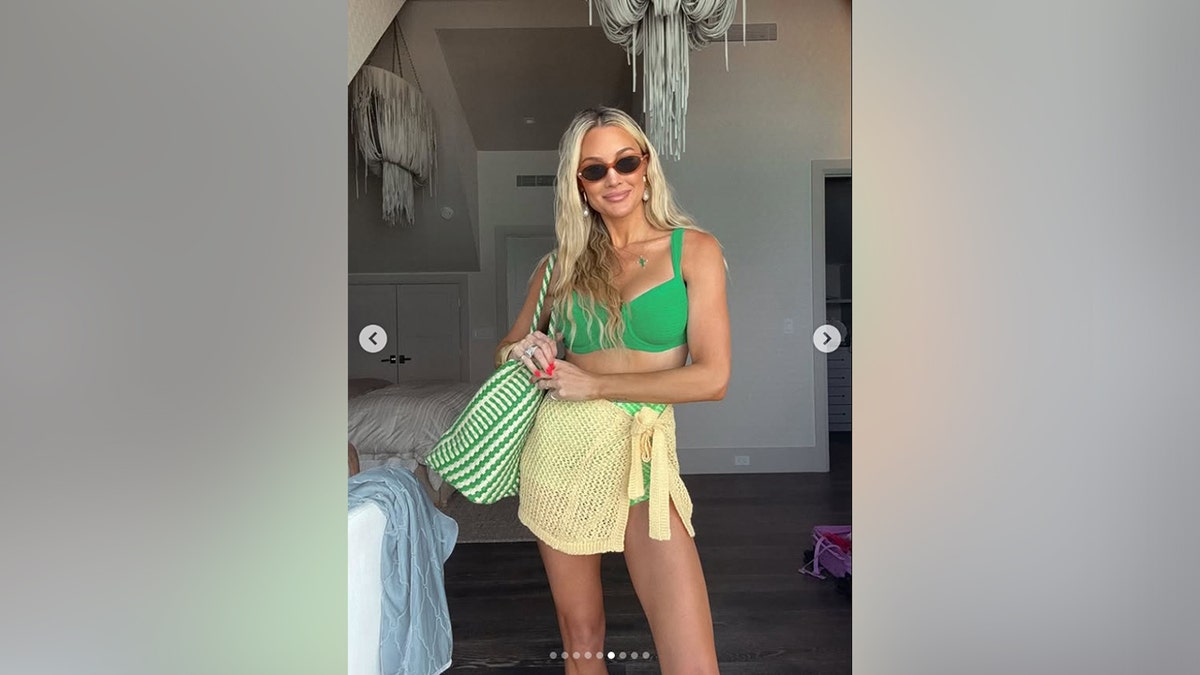 Brittany Aldean carrying a green and white beach bag in a hotel room