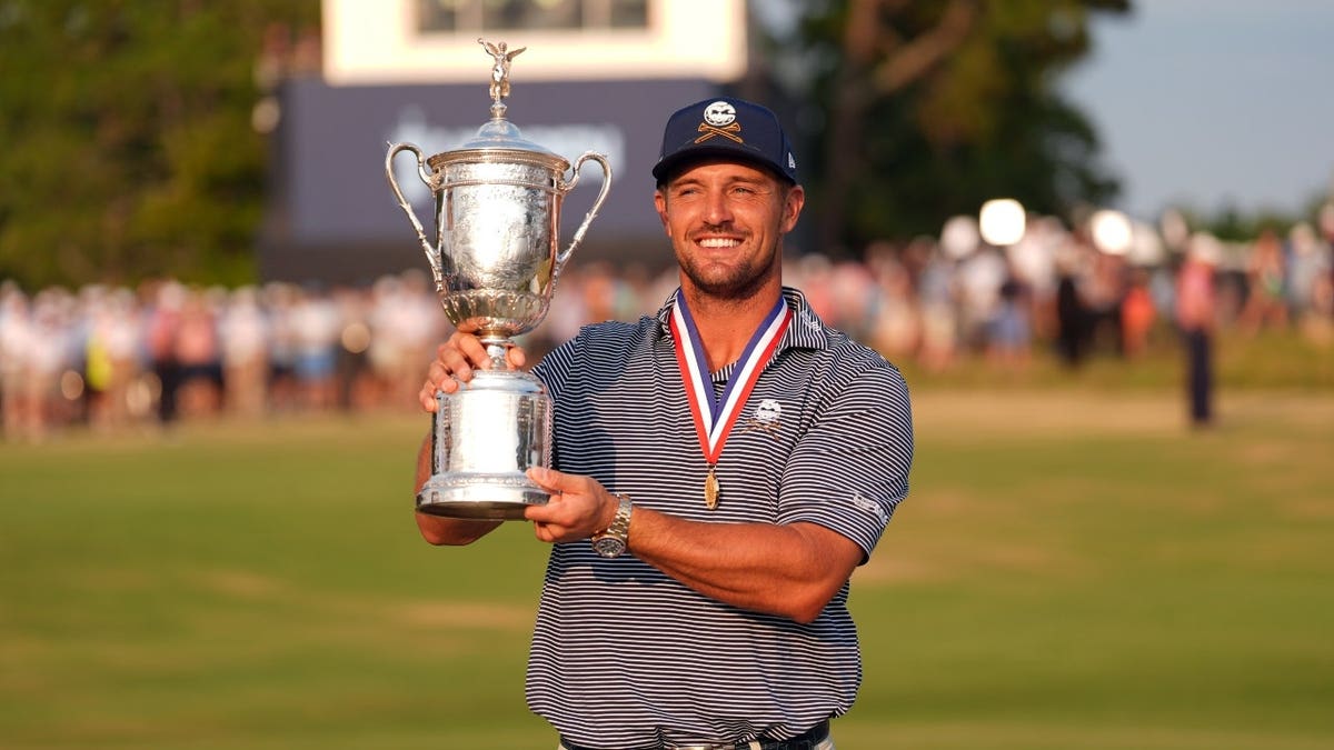 Bryson DeChambeau celebrating with trophy on golf course.