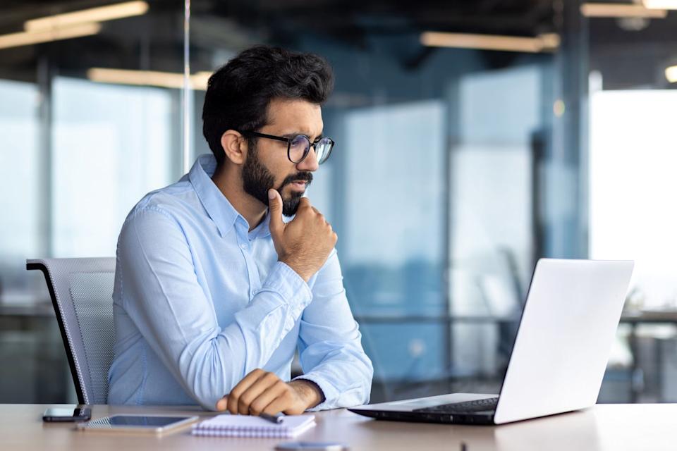 A seated investor is thinking while staring at a laptop screen. 