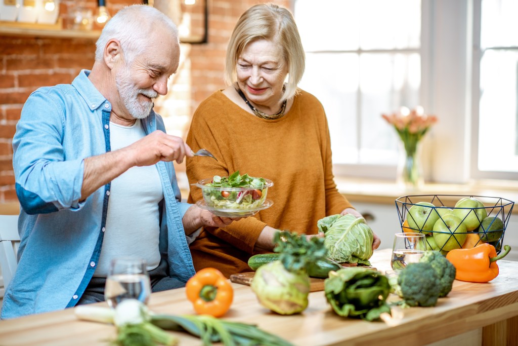 A cheerful senior couple preparing healthy food together in their kitchen.