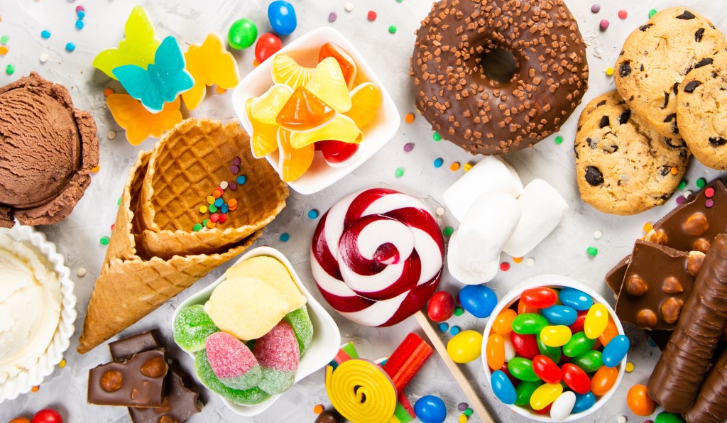 An assortment of colorful candies and sweets including chocolate, donuts, cookies, lollipops, and ice cream.