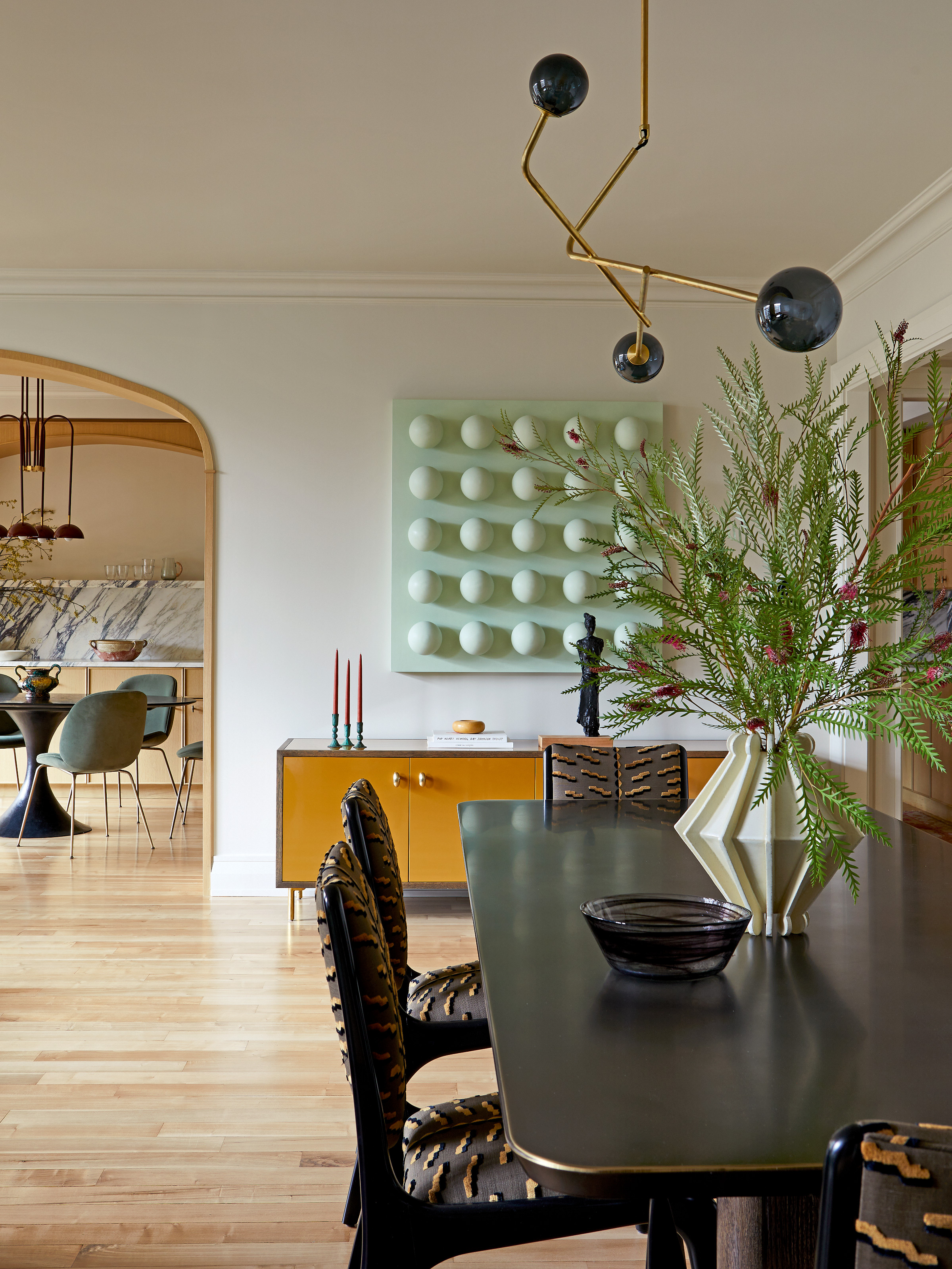Black dining table with gold edge, black dining chair with black and gold patterned upholstery, yellow sideboard and mint green 3D artwork