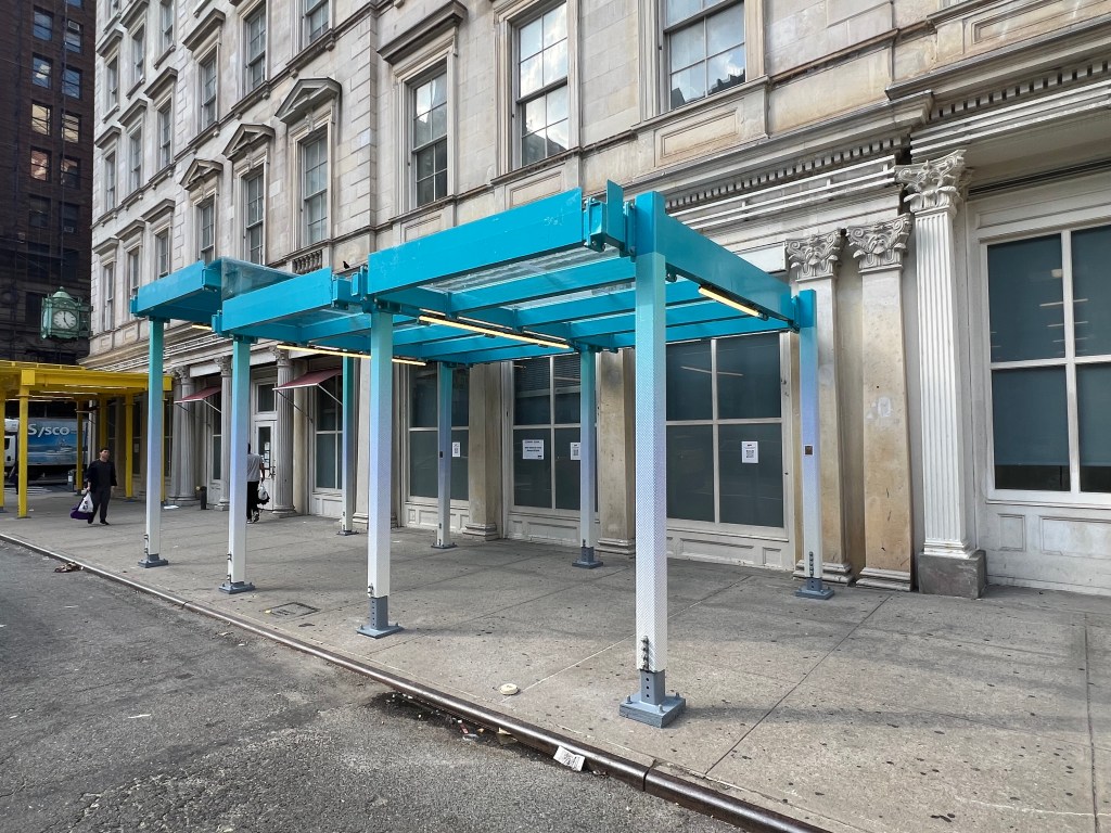 Models of proposed sidewalk sheds in teal and yellow on a city street.