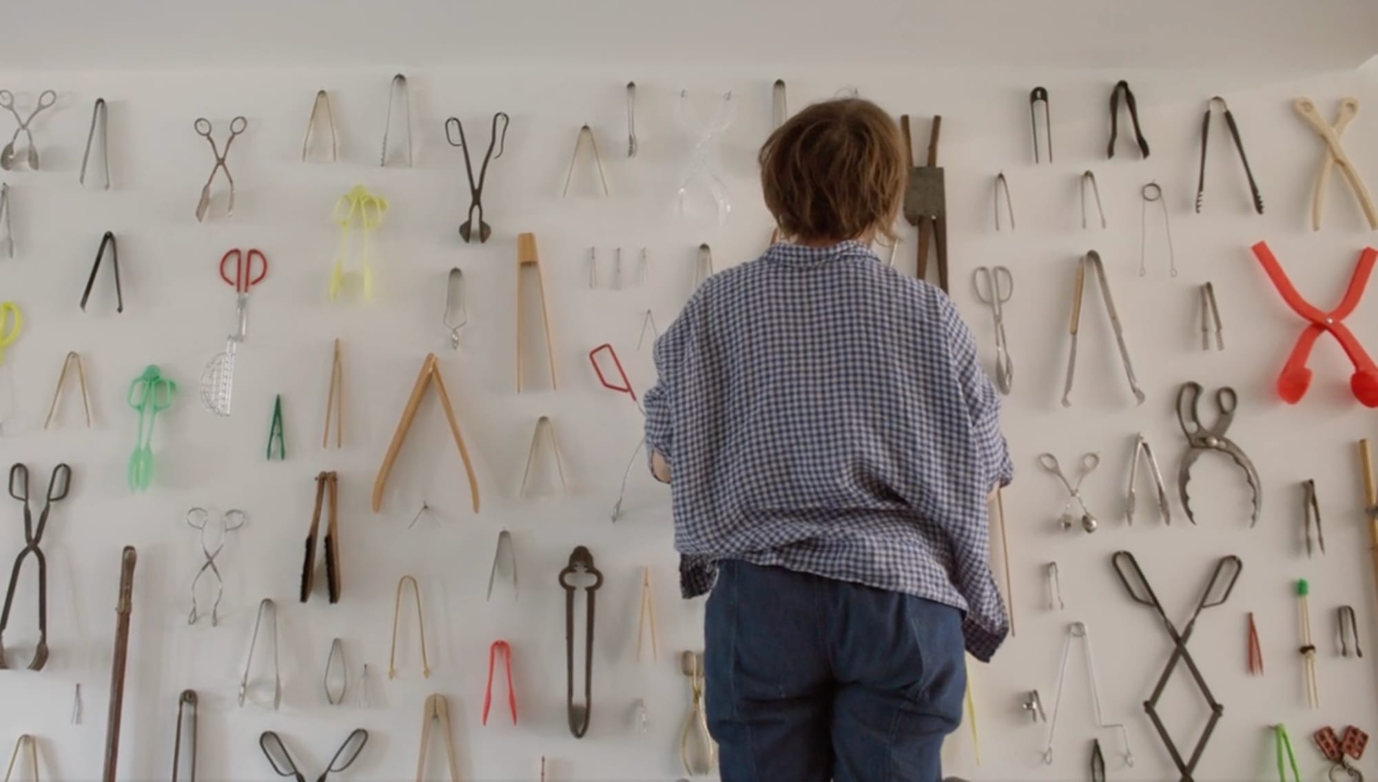 a woman with her back to the viewer looking at an installation of tongs
