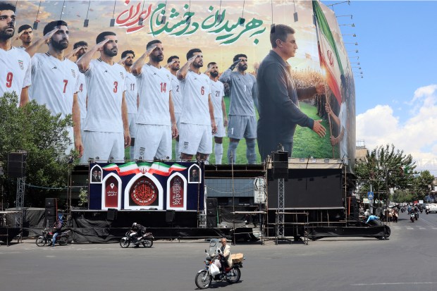 People on motorbikes ride past a billboard supporting Iran's national soccer team for the 2026 World Cup, on a building in Tehran on May 18, 2026. (Getty-AFP)
