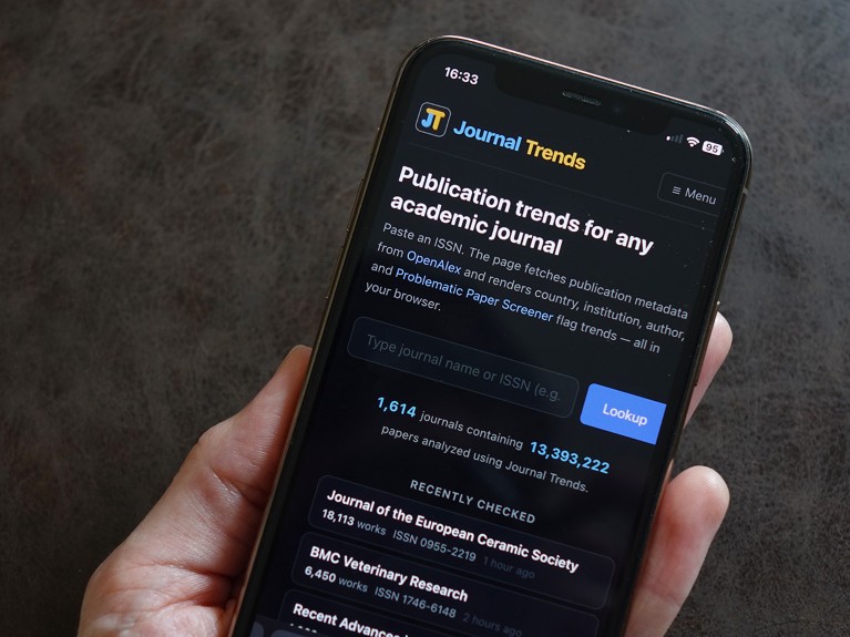 Close-up view of a smartphone being held in someone's hand and the Journal Trends website visible on the screen.