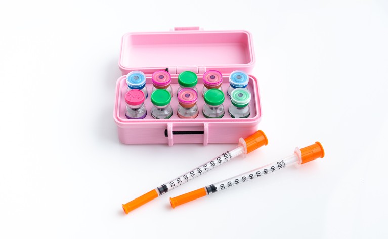A pink box containing vials of peptides along with two syringes laying in front of the box.