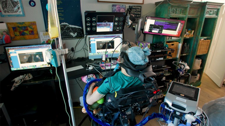 Casey Harrell using the brain-computer interface at his home. He is seated in his wheelchair and two wires can be seen attached to his head.
