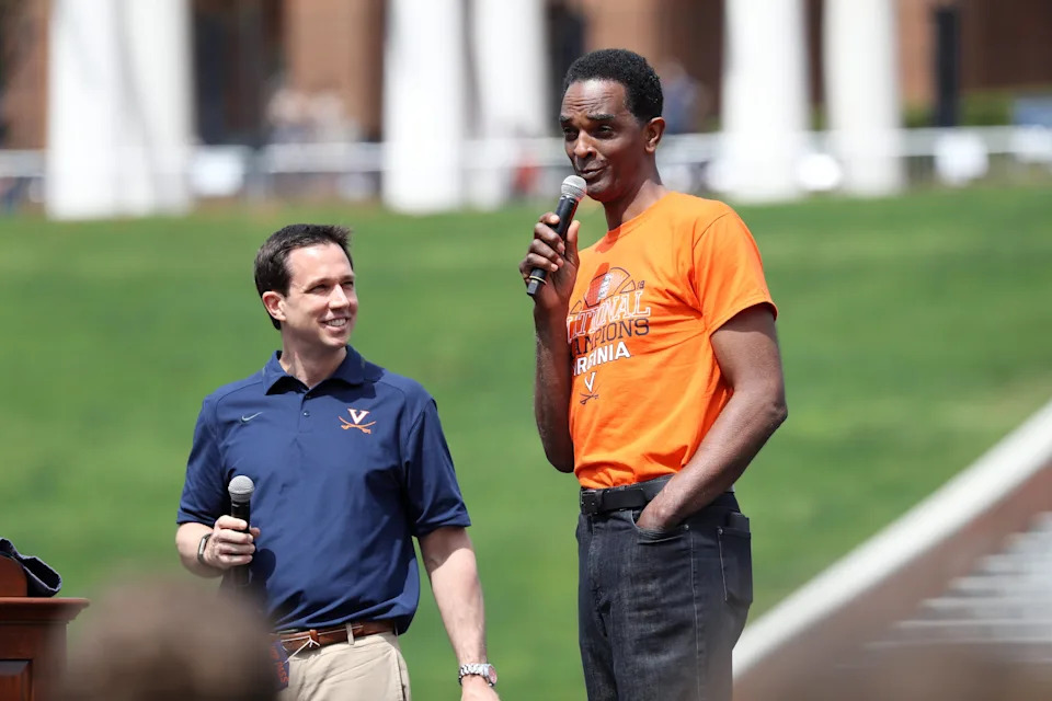 Two people speaking at an outdoor sports event; one wearing a casual polo, the other in a graphic T-shirt