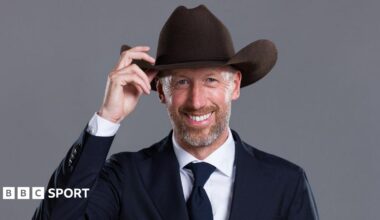 Graham Potter poses for the camera, wearing a suit while touching the brim of a cowboy hat