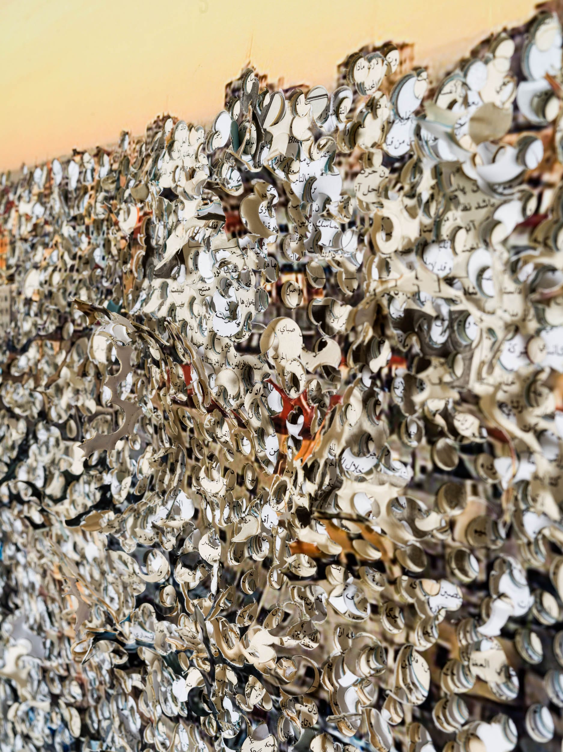 A detail of a large paper collage artwork with numerous punch-cut holes creating a texture, each also an aperture with an individual image inside