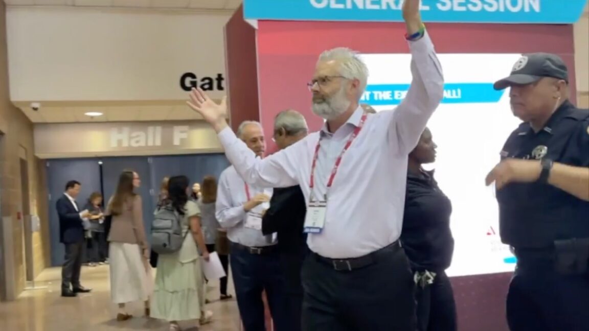 Police escort Dr. Steven Kahn out of a medical conference in New Orleans for handling out copies