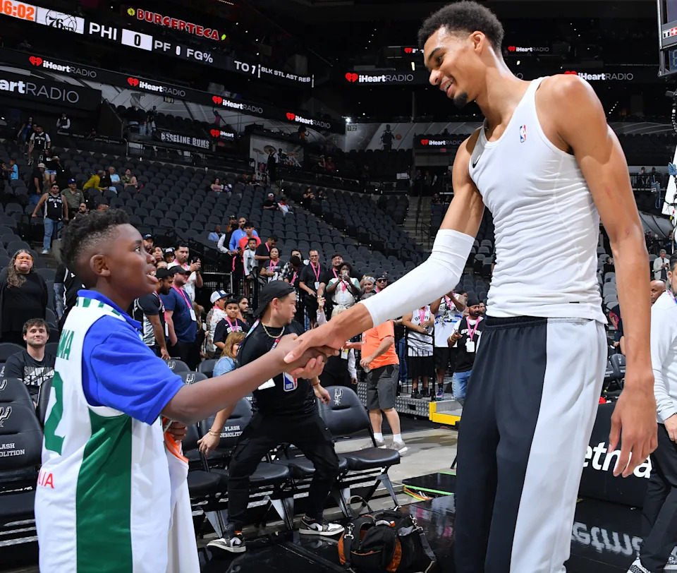 Basketball player in a tank top shakes hands with a young fan wearing a sports jersey after a game in an arena