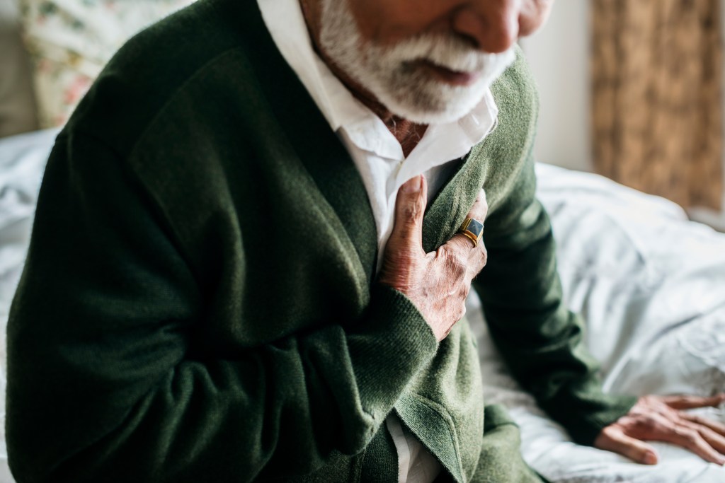 An elderly Indian man holding his chest due to heart problems.