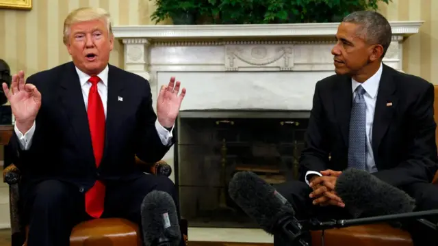 Donald Trump and Barack Obama in the Oval Office in 2016, three boom microphones for television broadcasts are held out in front of them.