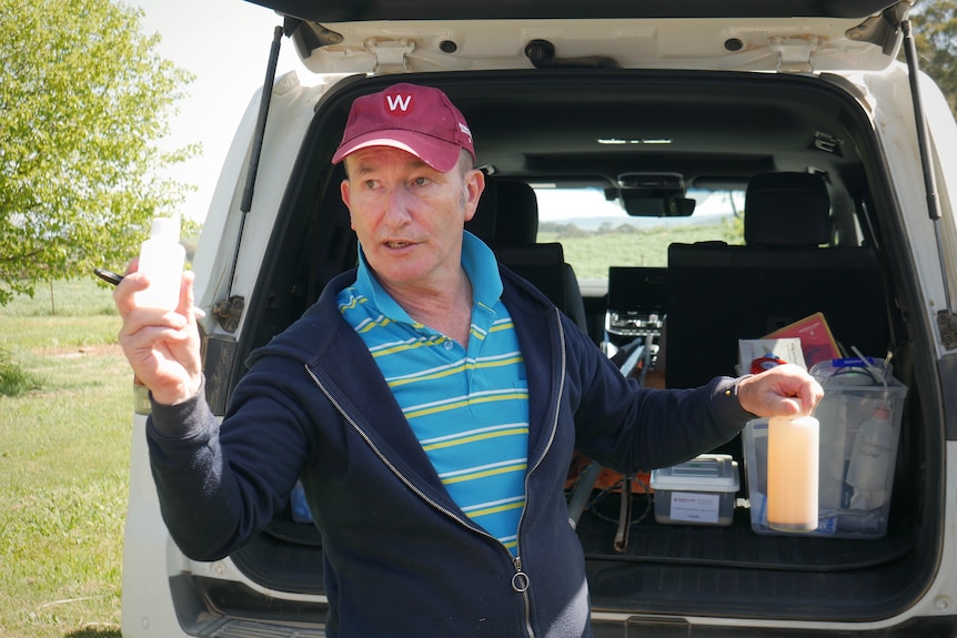 A man stands near the boot of a car holding sample bottles