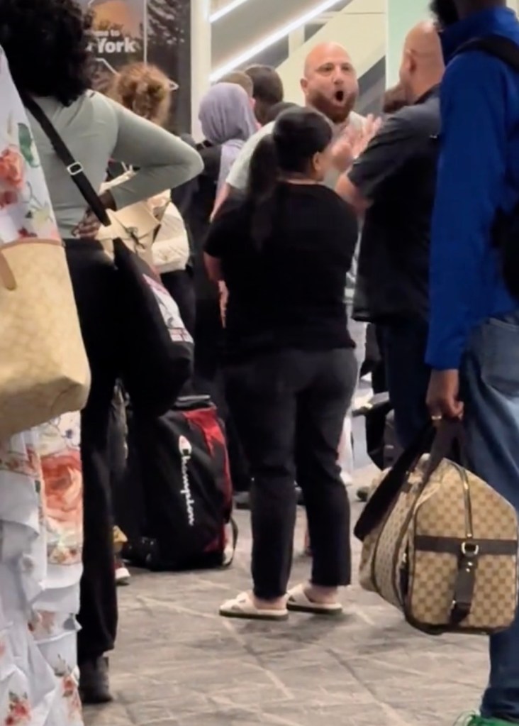 A bald man with an open mouth appears to be yelling at other people in an airport or public space.