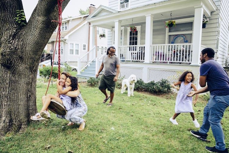 A group of people are playing outside in a front yard of a house.