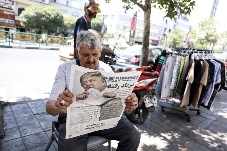 A man sitting outdoors reads a newspaper.