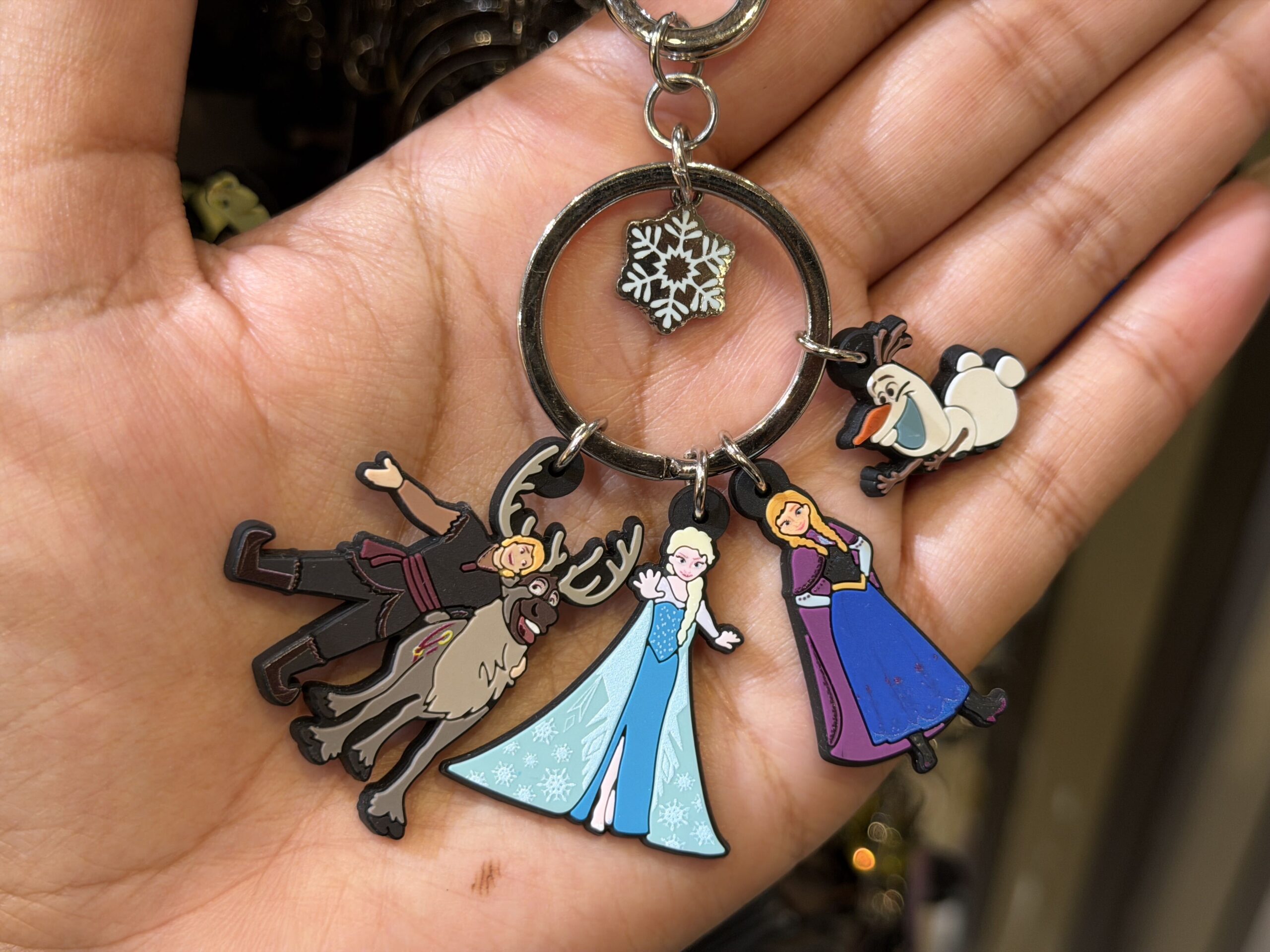 Five characters from Frozen are represented on four separate dangling charms on this keyring set. There are Kristoff and Sven, Elsa, Anna, and Olaf. A single white snowflake hangs inside the center ring.