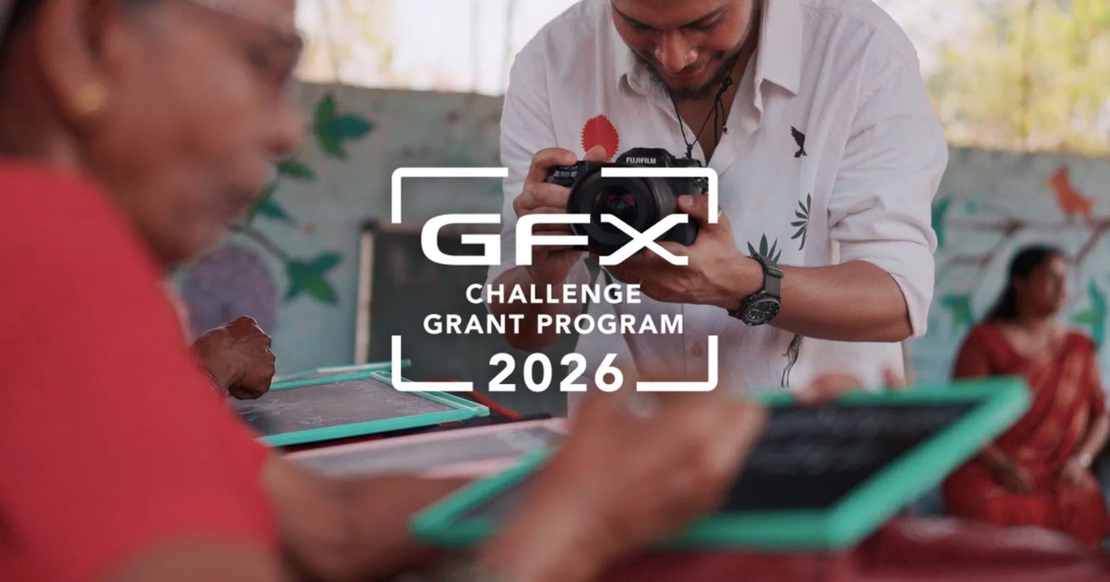 A photographer takes pictures of people writing on small chalkboards, with the text “GFX Challenge Grant Program 2026” overlaid in the center of the image.