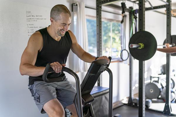 A fit mature man smiles while doing a cardio workout on a stationary bike.