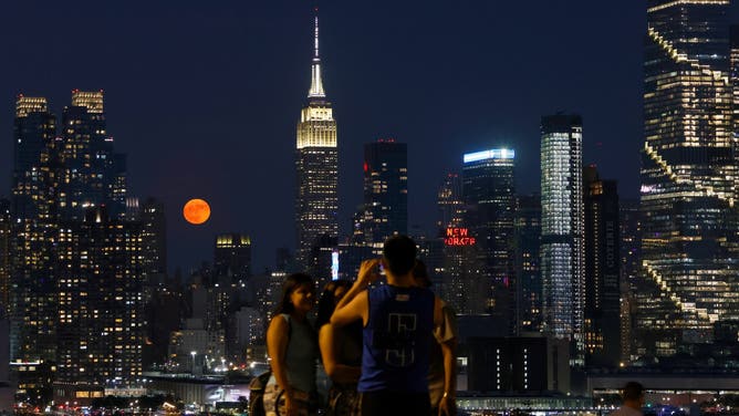 WEEHAWKEN, NJ - JUNE 21: The full Strawberry Moon rises behind the Empire State Building in New York City as people as people have their picture taken in a park on June 21, 2024, in Weehawken, New Jersey.