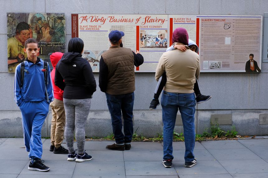 A family reads the signage about slavery on an outdoor exhibit at Independence National Historical Park in Philadelphia, Pennsylvania, on October 24, 2025.