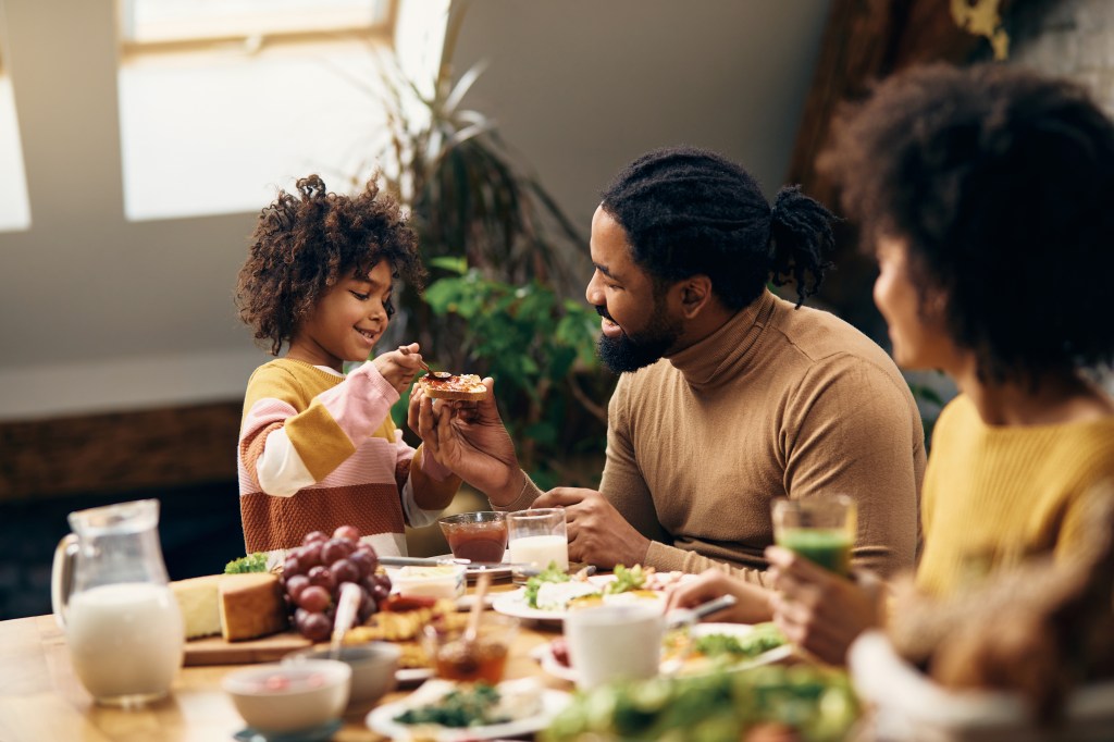 A happy family of three, an African American mother, father and daughter eating breakfast.