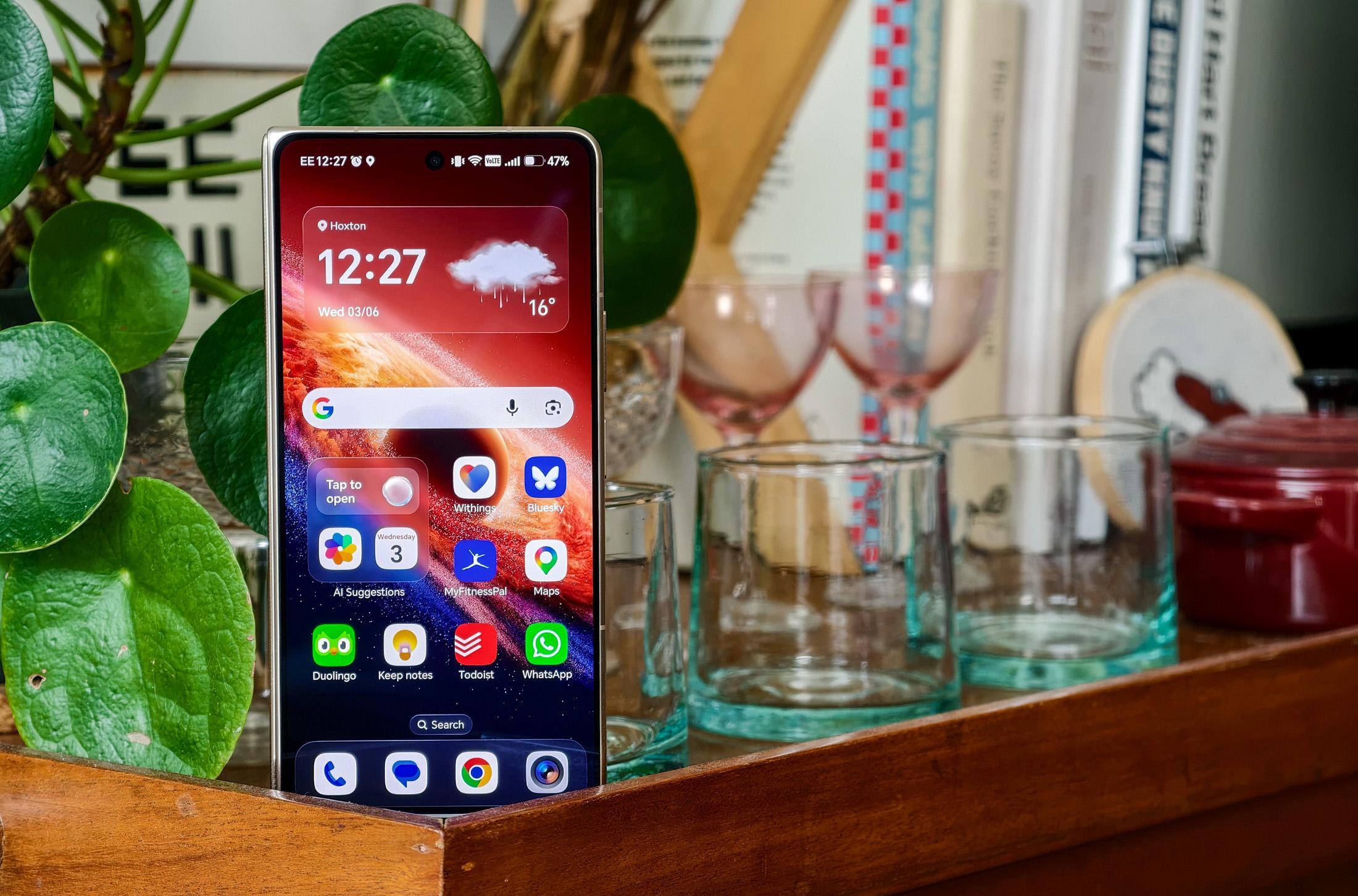 Photo of Honor Magic V6 on a wooden trolley with a pot plant and glassware, closed but showing the homescreen