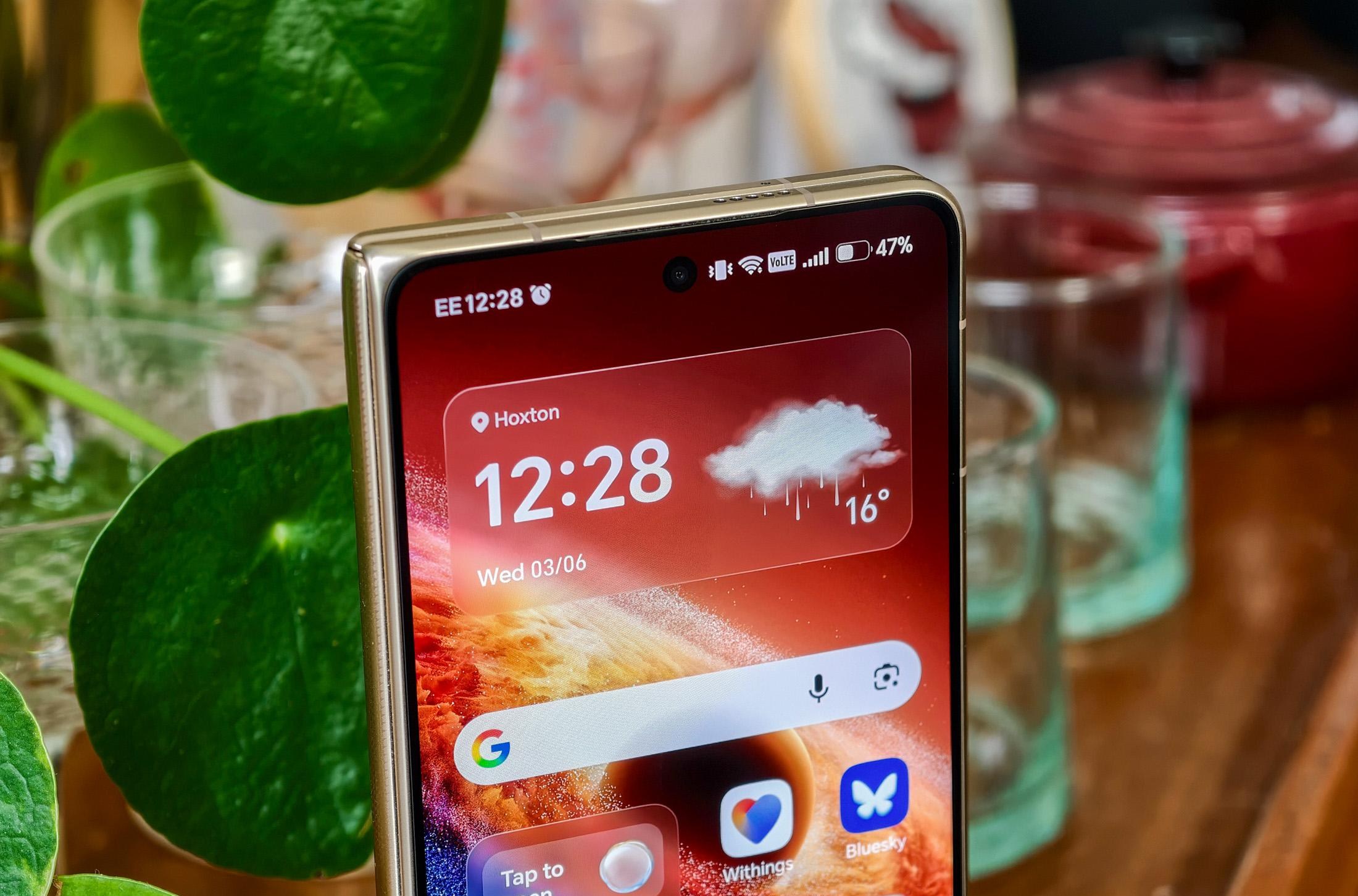 Photo of Honor Magic V6 on a wooden trolley with a pot plant and glassware, closed but showing the top of the homescreen