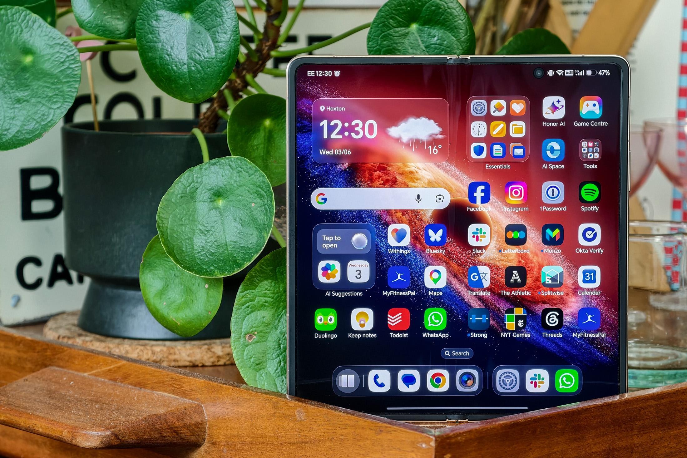 Photo of Honor Magic V6 on a wooden trolley with a pot plant and glassware, open to show the homescreen