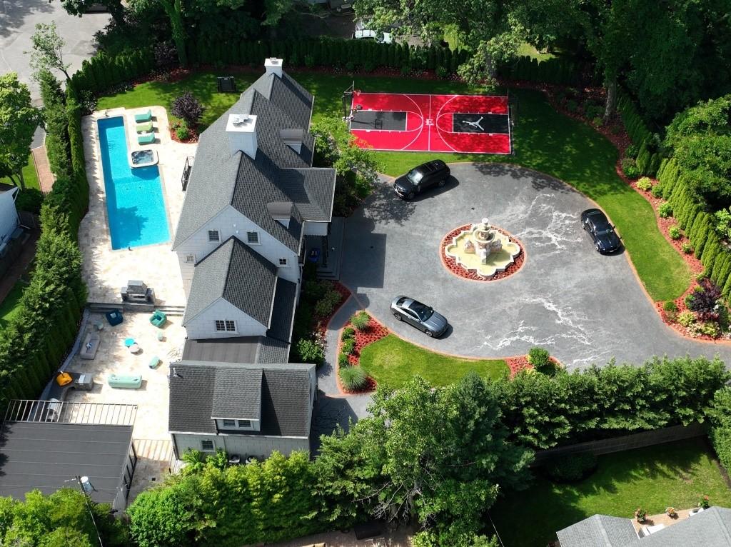 Aerial view of the opulent home of Nduka Lewis Ekpenyong in Hewlett, New York, including a pool, hot tub, outdoor lounge, a red basketball court, and a large driveway with multiple cars.