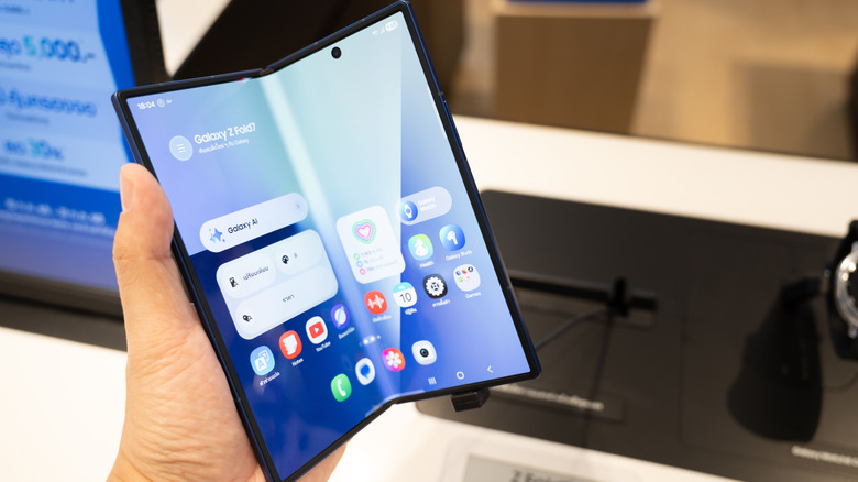 Hand holding an unfolded Samsung Galaxy Z Fold phone with the home screen open.
