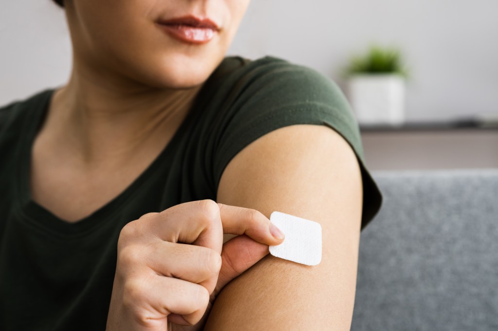 A woman applying a contraception patch to her upper arm.