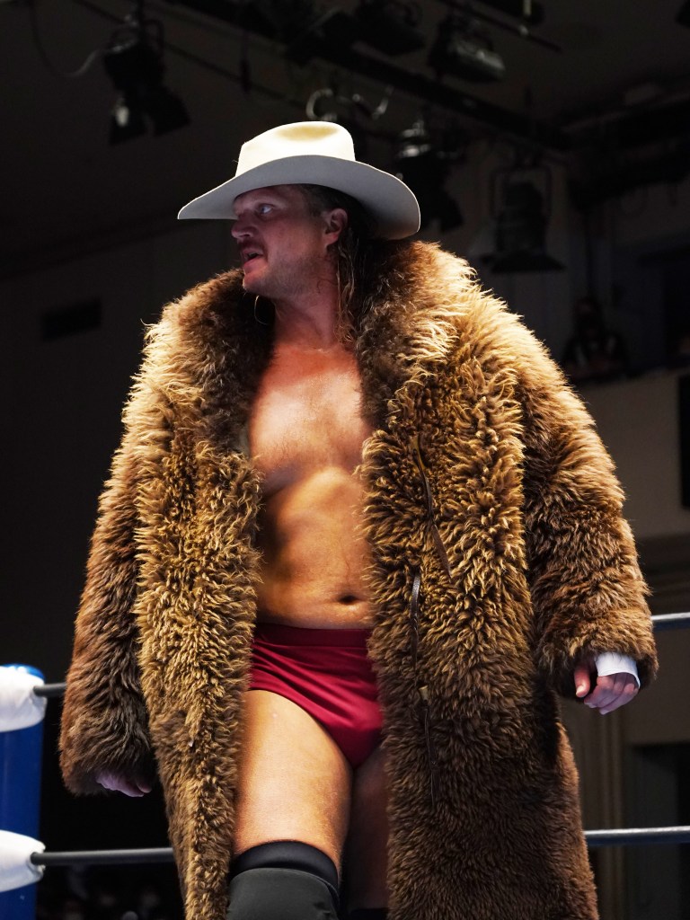 Joe Doering enters the ring wearing a white cowboy hat and a long brown fur coat.