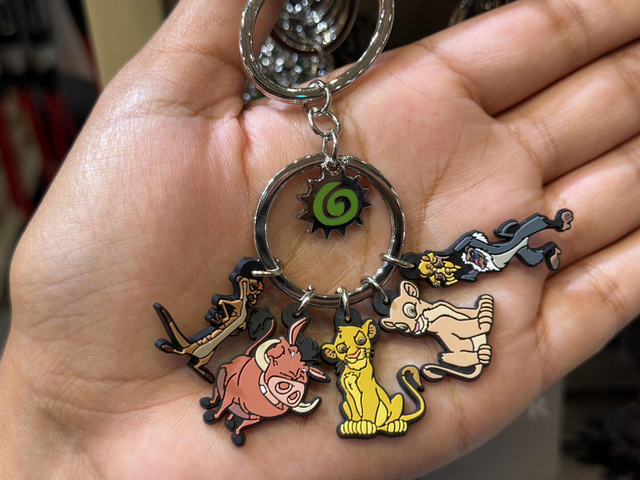 This keychain set includes five characters (technically six) from The Lion King. They are Timon, Pumbaa, Simba, Nala, and Rafiki holding baby Simba. Hanging in the center ring is what appears to be a sun with a swirl in it.