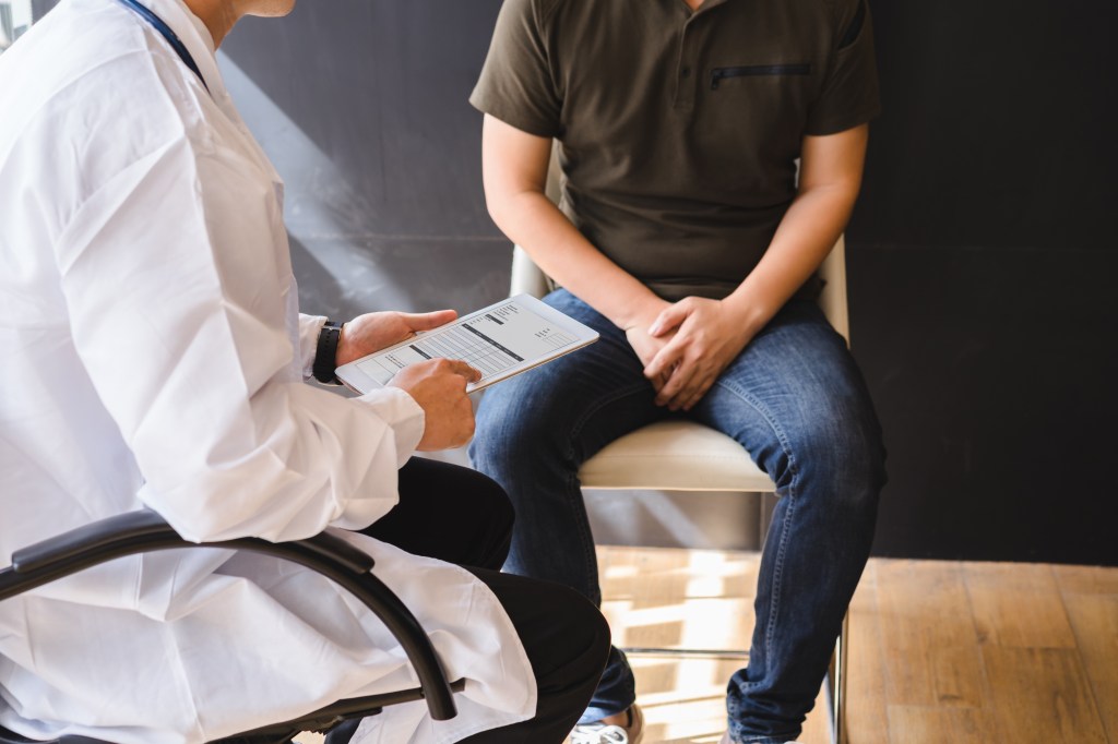 A doctor in a white coat shows a male patient a report on a tablet.