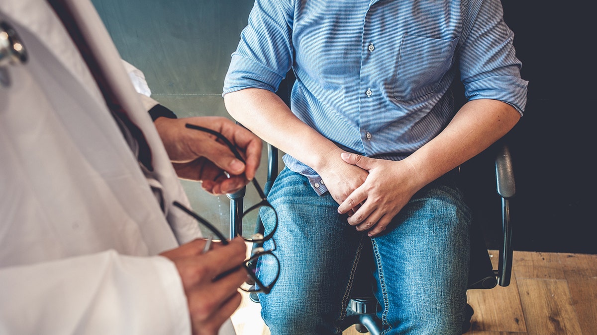 Doctor holding glasses consulting with man about reproductive health in medical office