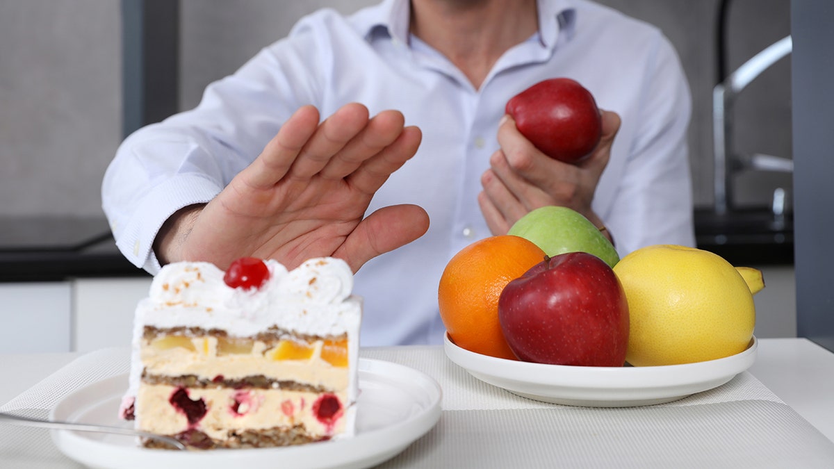 Man refusing to eat unhealthy cake and choosing fruits for dessert.