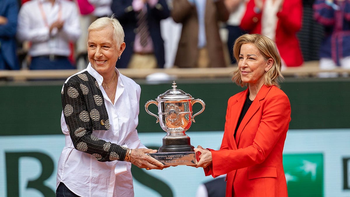 Martina Navratilova and Chris Evert presenting trophy to Iga Świątek on tennis court