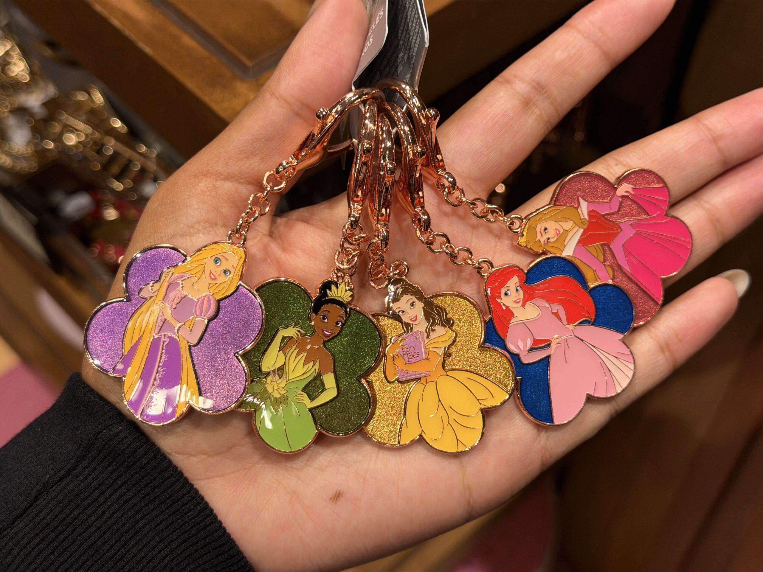 Unlike the other keychains featured here, this one is metal. All five princesses are shown against a glittery flower in a corresponding color. They are Rapunzel, Tiana, Belle, Ariel, and Aurora.