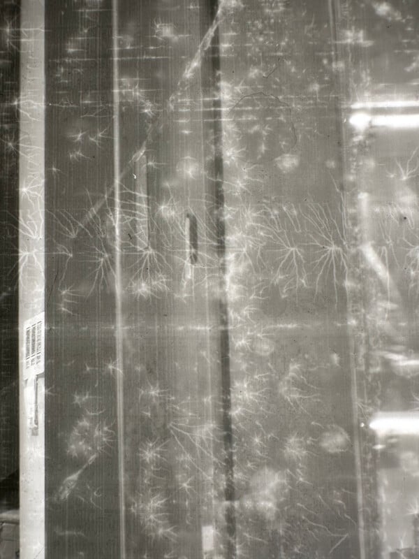 Faint white lines and starburst patterns appear on a scratched, reflective gray surface with vertical lines and a barcode on the left side.
