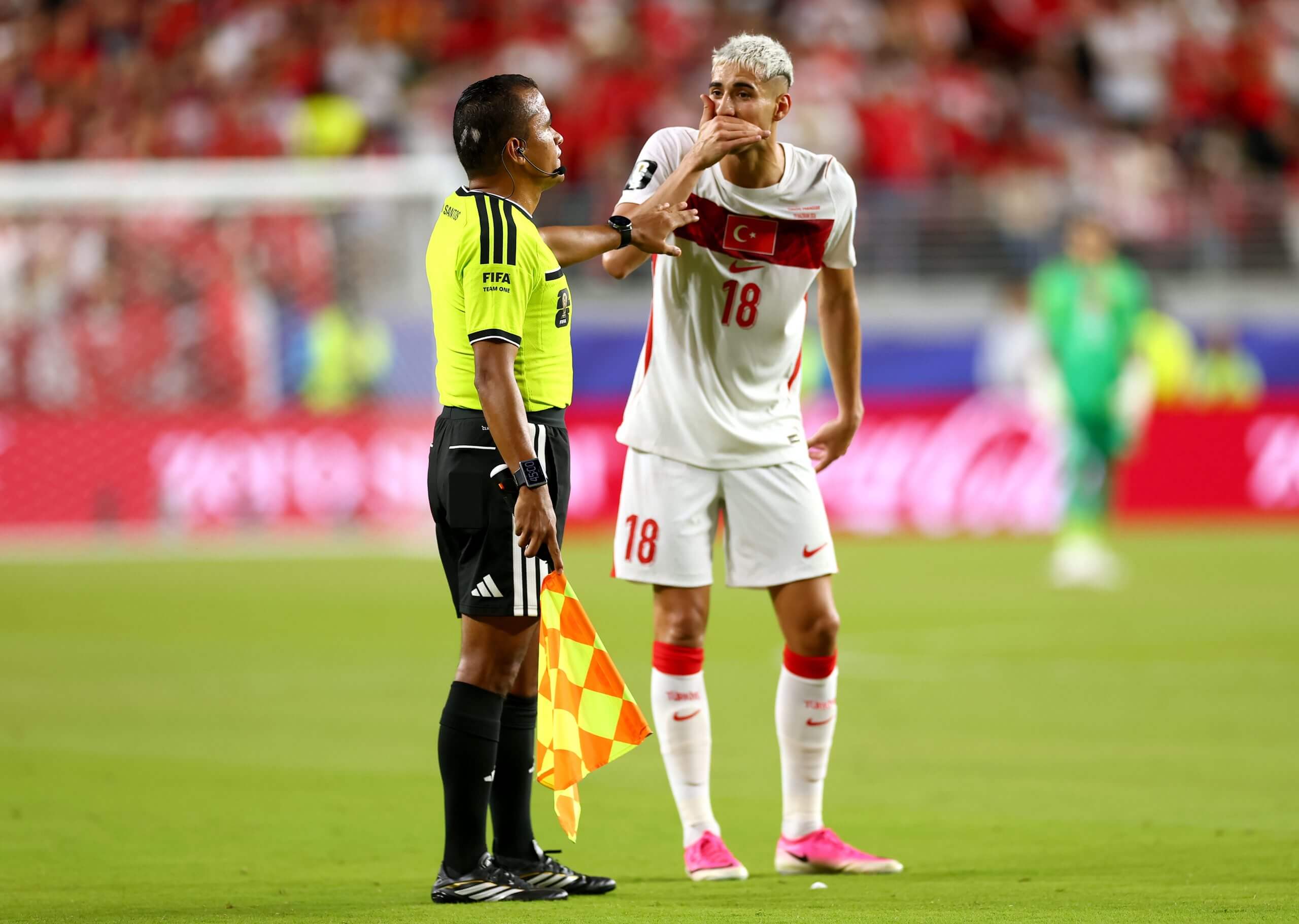Muldur replicating Almiron's mouth-covering gesture to an assistant referee